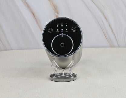 The Jarhead Aromatics Cold Air Diffuser – Portable & Rechargeable – features a sleek cylindrical design with a black control panel and buttons, displayed on a minimalist silver stand against a light marbled background for an earthy, elegant look.