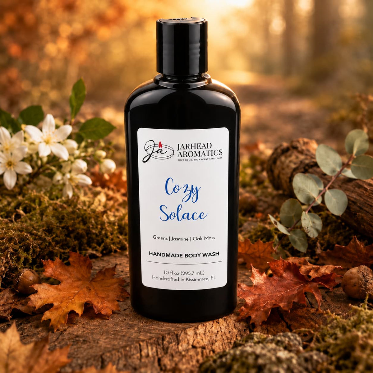 A bottle of Jarhead Aromatics Cozy Solace Handmade Body Wash, featuring notes of fresh greens, jasmine, and oak moss, rests on a forest floor scattered with autumn leaves and flowers beneath gentle sunlight.