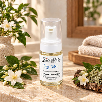 A bottle of Cozy Solace Handmade Foaming Hand Soap with a clear pump lid, surrounded by white jasmine flowers and greenery on a countertop.
