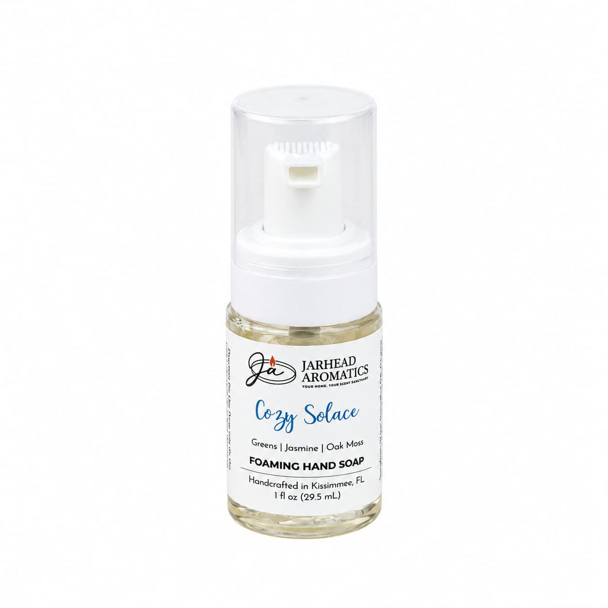 A small, clear plastic bottle of Cozy Solace Handmade Foaming Hand Soap with a white pump dispenser and a label featuring the botanical fragrance notes of greens, jasmine, and oak moss.