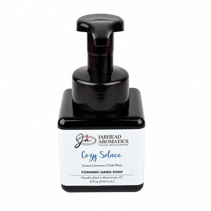 Square dark bottle of Cozy Solace Handmade Foaming Hand Soap with a black pump dispenser and a label reading Greens | Jasmine | Oak Moss.