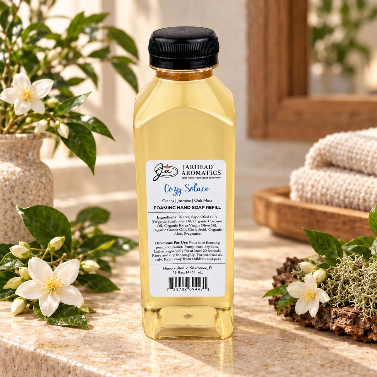 A clear plastic bottle of Cozy Solace Handmade Foaming Hand Soap with a white label detailing ingredients and directions, surrounded by white flowers and moss.