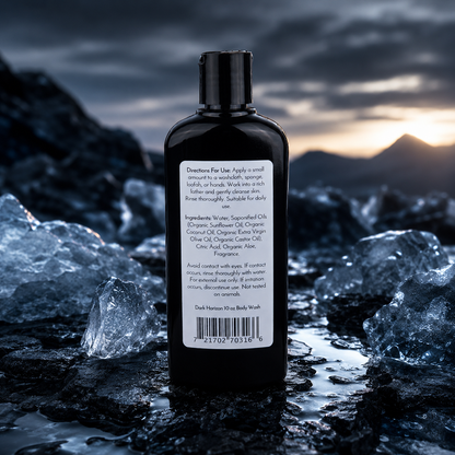 A black bottle of Jarhead Aromatics Dark Horizon Handmade Body Wash with a white label stands on icy rocks before dramatic mountains. The label highlights its organic aloe and plant-based oils, plus directions for use.