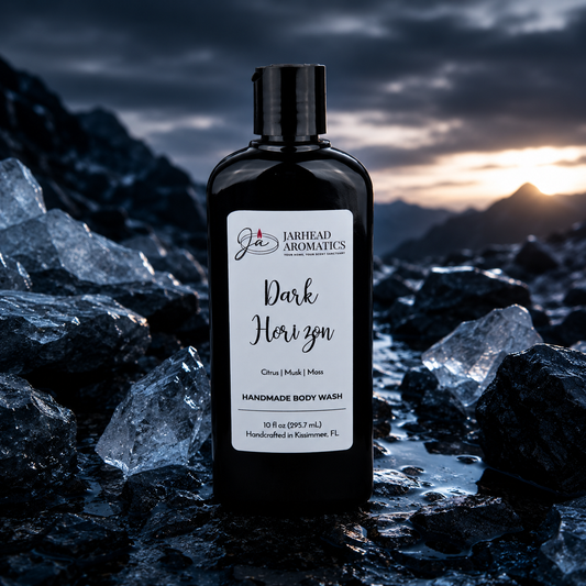 A bottle of Jarhead Aromatics Dark Horizon Handmade Body Wash with organic aloe and plant-based oils rests among black rocks and ice shards, set against a dramatic sunset and mountain backdrop.