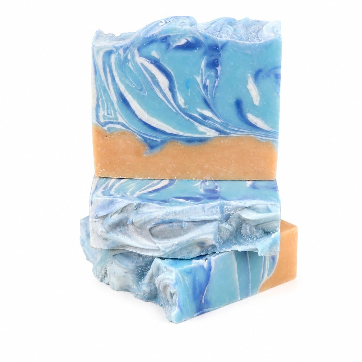 Three rectangular bars of Jarhead Aromatics Driftwood + Sea Salt Handmade Coconut Milk Artisan Soap, featuring blue, white, and beige marbled swirls, are stacked on a white background. The bottom bar lies flat while the others stand upright—highlighting the unique patterns that make this coastal bar soap truly one-of-a-kind.