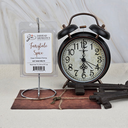 A package of Jarhead Aromatics Fairytale Spice Soy Wax Melt | Warm Gingerbread & Holiday Spice Wax Melts sits beside a vintage black alarm clock, old keys, and a twine-wrapped envelope on a light marble background.