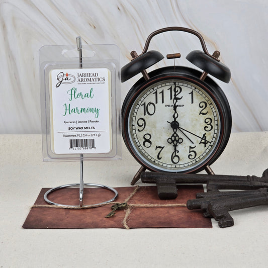 A vintage black alarm clock sits beside Jarhead Aromatics’ Floral Harmony Soy Wax Melt, filling the space with an elegant white floral scent. Large decorative keys and an envelope rest on the table against a light marbled background.