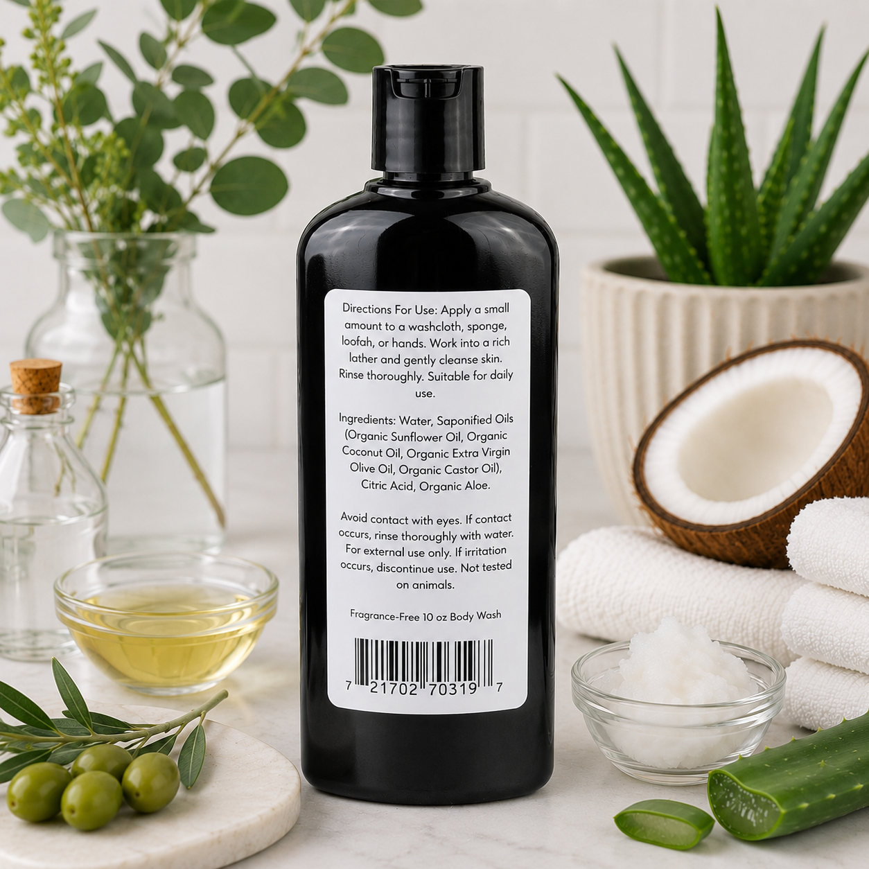A black bottle of Jarhead Aromatics Fragrance-Free Handmade Natural Body Wash with organic aloe and plant-based oils sits on a white surface, surrounded by olive oil, coconut, green leaves, aloe vera, a white towel, and a glass bowl.