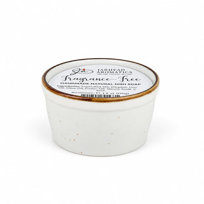 A white ceramic ramekin filled with a Fragrance-Free Handmade Natural Solid Dish Soap | Kitchen Cleaning Bar, featuring a label that lists the ingredients.