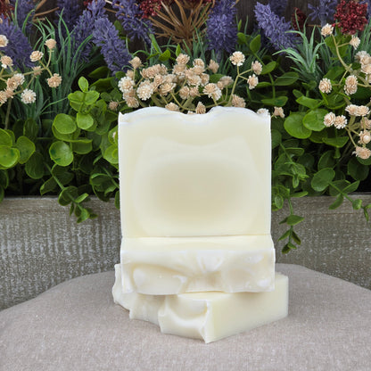 Three handmade Fragrance-Free Natural Tallow Artisan Soaps by Jarhead Aromatics are stacked on a beige cloth, surrounded by flowers and greenery, highlighting their gentle, unscented formula for sensitive skin.