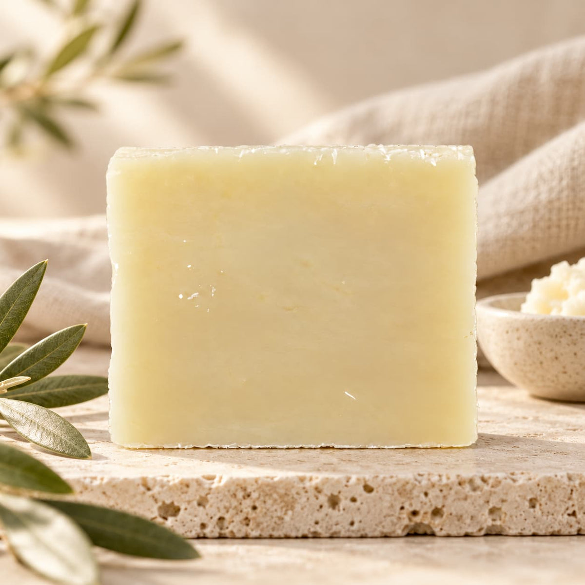 A rectangular bar of Jarhead Aromatics Fragrance-Free Natural Handmade Soap sitting on a stone surface next to olive leaves.