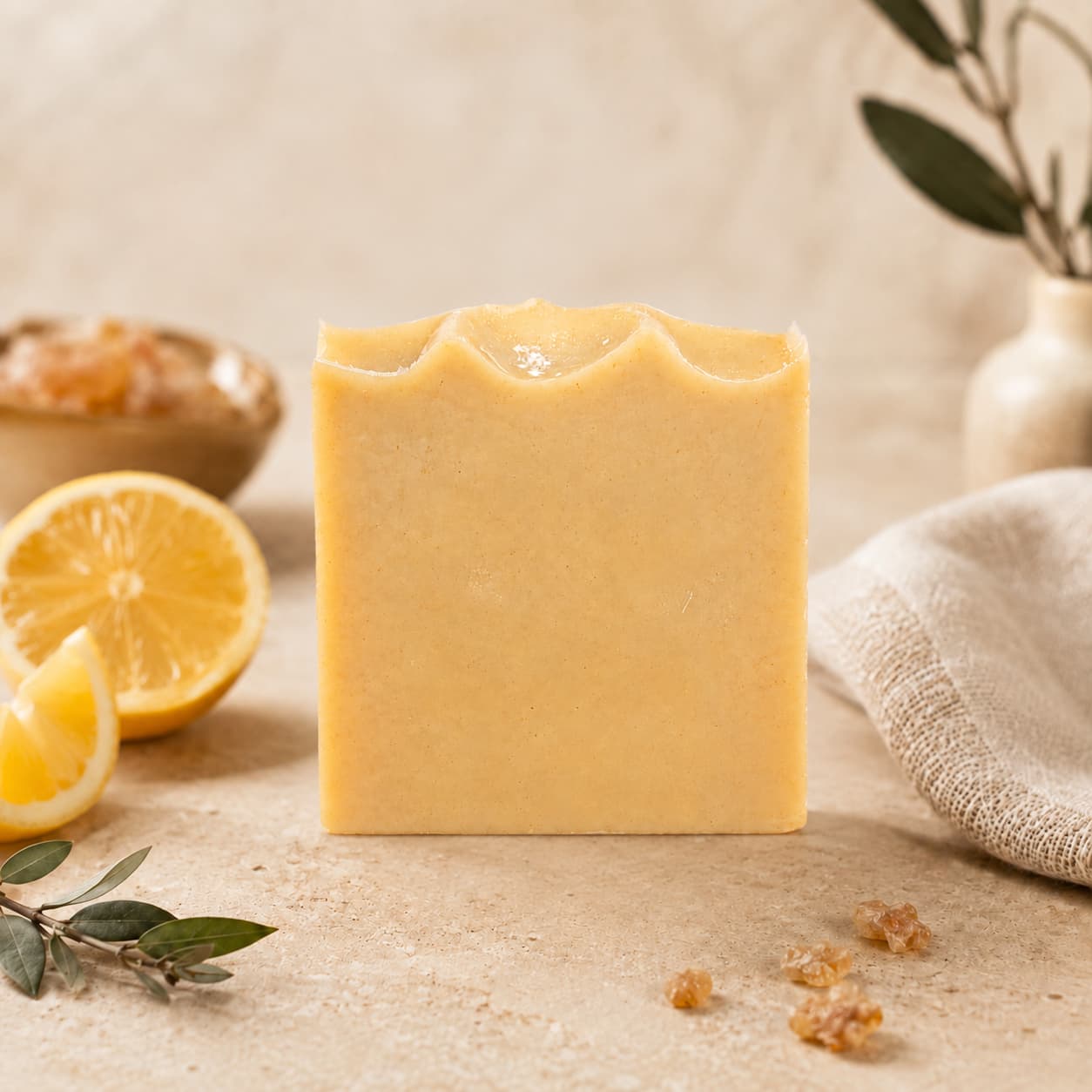 A bar of Jarhead Aromatics Frankincense + Citrus Handmade Natural Tallow Artisan Soap stands upright on a beige surface, surrounded by lemon slices, a small bowl, green leaves, and a white cloth, set against a neutral background.