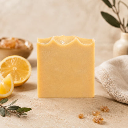 A bar of Jarhead Aromatics Frankincense + Citrus Handmade Natural Tallow Artisan Soap stands upright on a beige surface, surrounded by lemon slices, a small bowl, green leaves, and a white cloth, set against a neutral background.