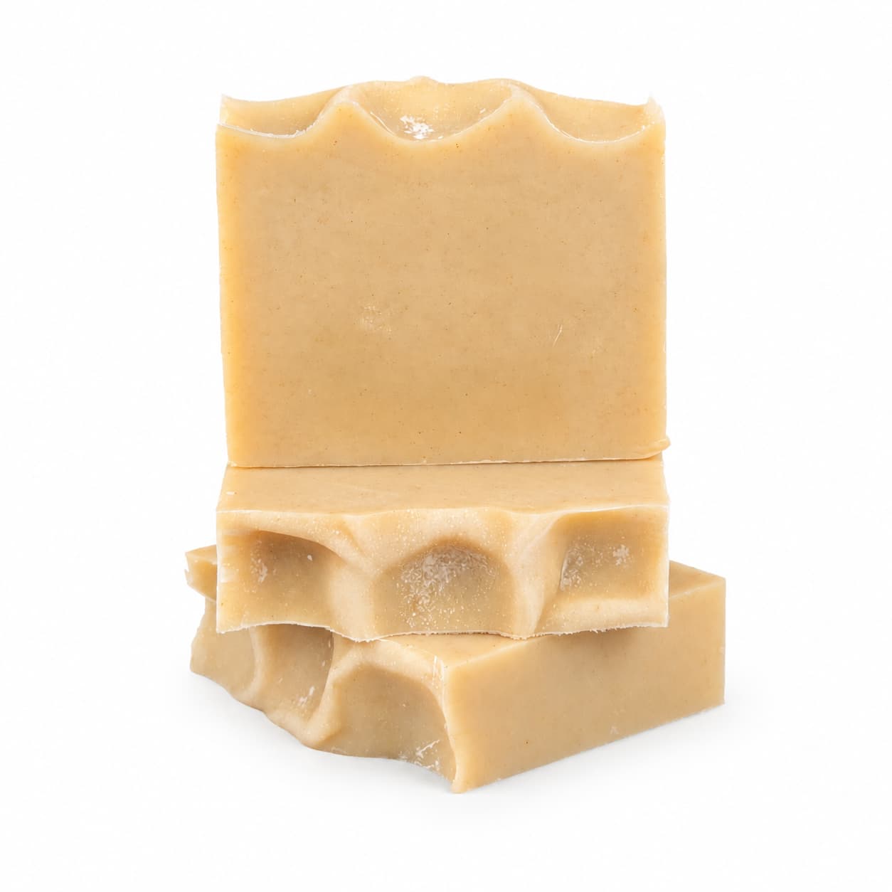 Three tan-colored bars of Jarhead Aromatics’ Frankincense + Citrus Handmade Natural Tallow Artisan Soap are stacked, with the top bar standing upright and the other two lying flat. The soap bars feature wavy, textured edges and a smooth surface, showcasing their artisan quality against a plain white background. This natural tallow soap highlights resinous frankincense and bright citrus scents.