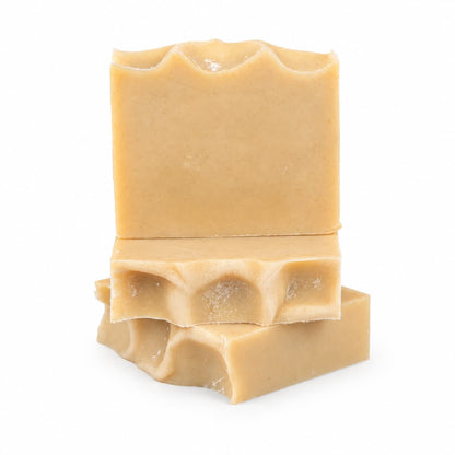 Three tan-colored bars of Jarhead Aromatics’ Frankincense + Citrus Handmade Natural Tallow Artisan Soap are stacked, with the top bar standing upright and the other two lying flat. The soap bars feature wavy, textured edges and a smooth surface, showcasing their artisan quality against a plain white background. This natural tallow soap highlights resinous frankincense and bright citrus scents.