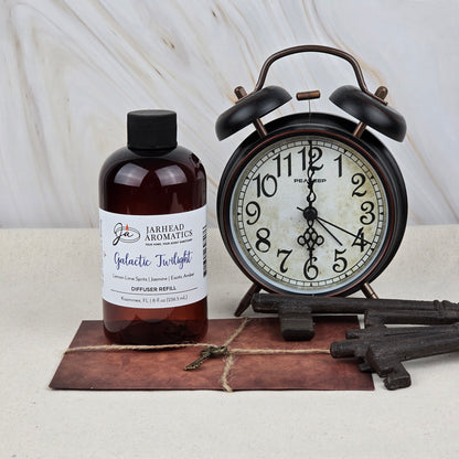 A bottle of Jarhead Aromatics Galactic Twilight Diffuser Refill (Amber, Jasmine & Sandalwood) sits beside a black alarm clock, three antique keys, and an envelope topped with a small key.