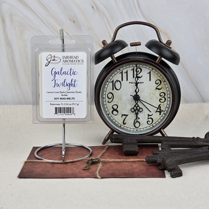 A pack of Jarhead Aromatics’ Galactic Twilight Soy Wax Melts (Amber Citrus & Sandalwood) sits next to a vintage black alarm clock at 10:15, with two large keys and a sealed brown envelope on a light background.