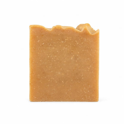 A rectangular bar of Ginger + Sweet Orange Handmade Natural Goat Milk Artisan Soap from Jarhead Aromatics, featuring a rough, uneven top edge, stands upright against a plain white background. This zesty citrus and warm ginger soap is carefully crafted to showcase its unique texture and wholesome, natural ingredients.