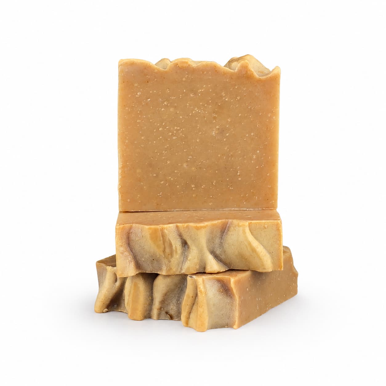 Two handmade Ginger + Sweet Orange Natural Goat Milk Artisan Soap bars by Jarhead Aromatics, with rich brown tones and uneven, textured tops, are stacked against a white background. Featuring a zesty citrus blend of sweet orange and warm ginger, these thoughtfully crafted soap bars include nourishing ingredients for the skin. The top bar stands upright while the other Handmade Goat Milk Soap rests flat beneath it.