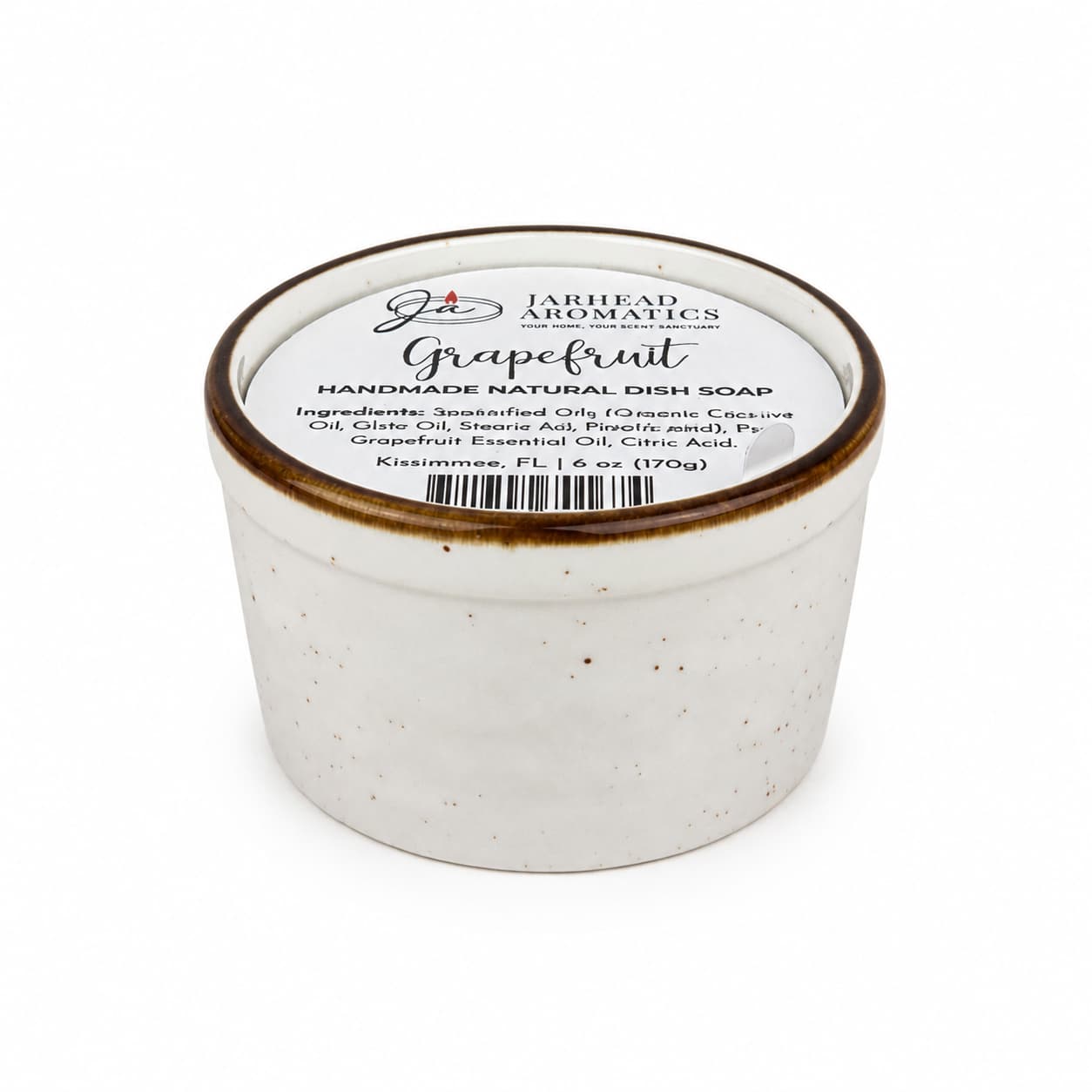 A white ceramic jar of Jarhead Aromatics Grapefruit Handmade Natural Solid Dish Soap | Citrus Kitchen Cleaning Bar with Grapefruit Essential Oil is photographed on a white background, its lid displaying an ingredient list. This plant-based, eco-friendly dish soap offers natural cleaning power paired with the invigorating aroma of grapefruit—an essential for any green kitchen.