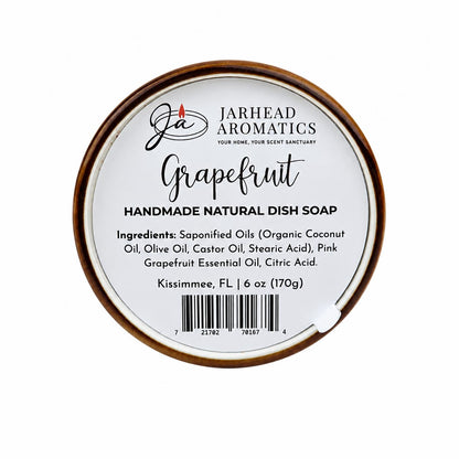 Round container labeled Jarhead Aromatics Grapefruit Handmade Natural Solid Dish Soap | Citrus Kitchen Cleaning Bar with Grapefruit Essential Oil. This plant-based dish soap lists ingredients and weight (6 oz/170g) on the label. The lid is wood-toned, and the text appears in black on a white background.