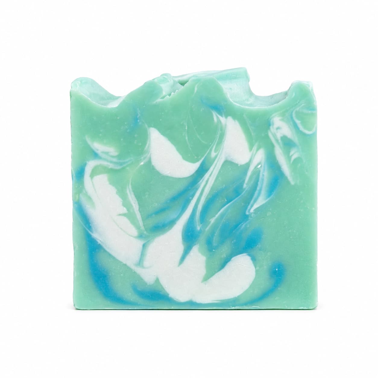 A rectangular bar of Jarhead Aromatics’ Honeysuckle + Jasmine Handmade Coconut Milk Artisan Soap features a green base with blue and white swirling patterns and a wavy, uneven top, creating a fresh floral garden look.
