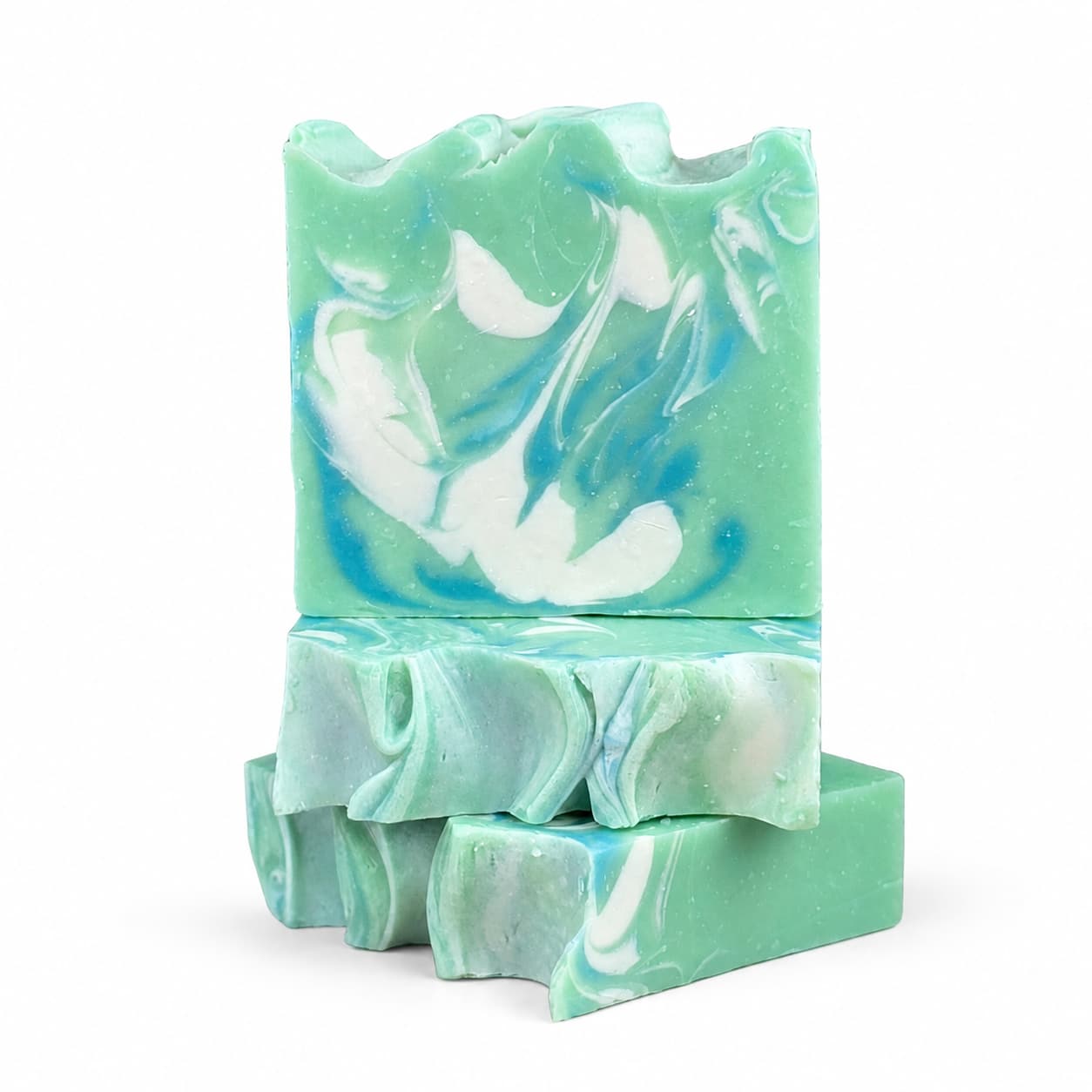 Three green Honeysuckle + Jasmine Handmade Coconut Milk Artisan Soap bars from Jarhead Aromatics, featuring white and blue marbled swirls, are stacked on a white background. The top bar displays a wavy, textured surface, highlighting the artistic and handcrafted nature of this fresh floral garden soap.