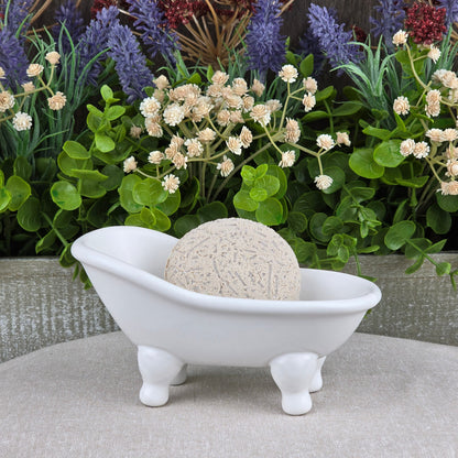 The Lavender Handmade Shampoo & Conditioner Bar by Jarhead Aromatics sits in a white ceramic tub on beige, surrounded by green plants and purple flowers—a tranquil scene ideal for zero-waste hair care enthusiasts.