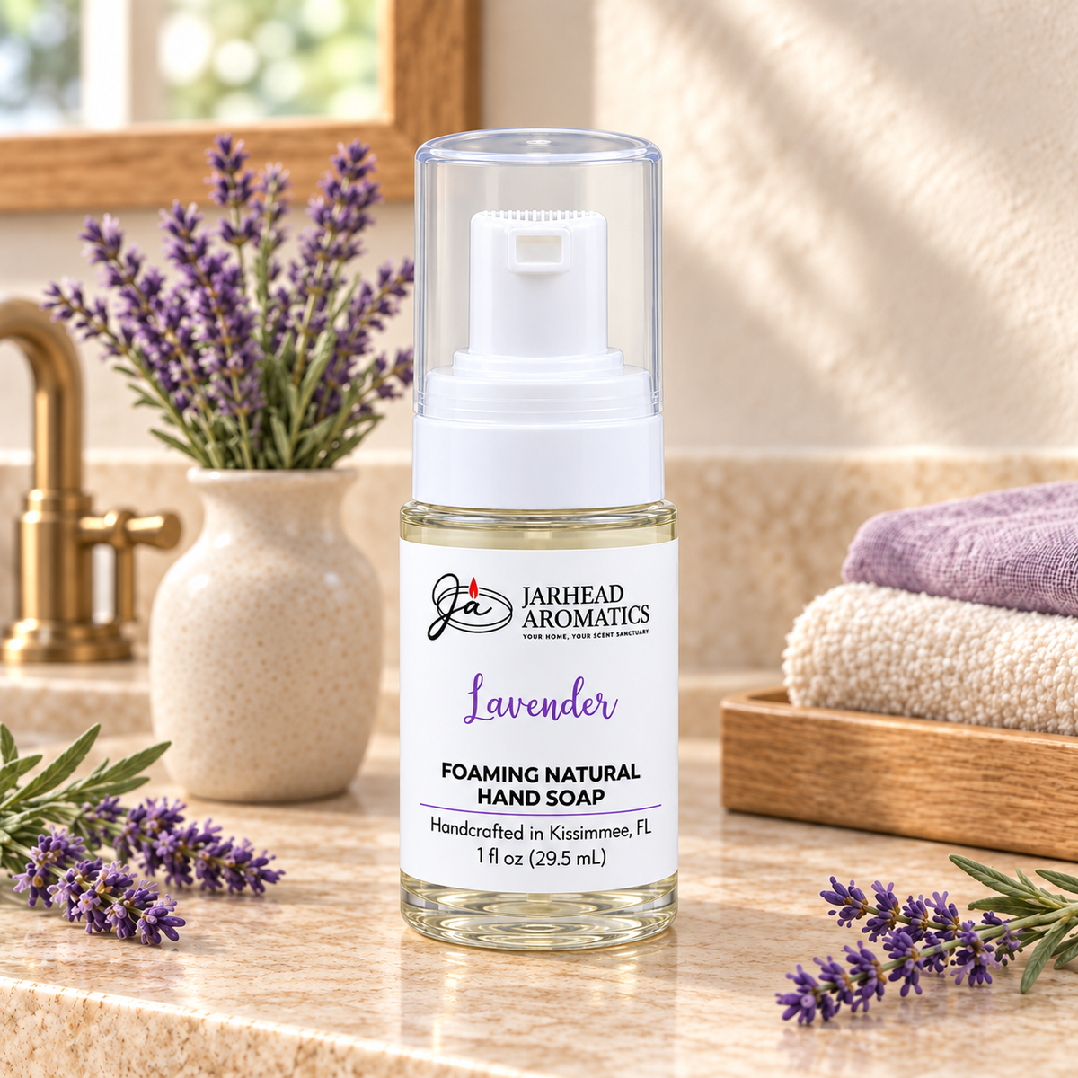 A bottle of Jarhead Aromatics Lavender Handmade Foaming Natural Hand Soap rests on a bathroom counter next to a vase of lavender and folded towels.