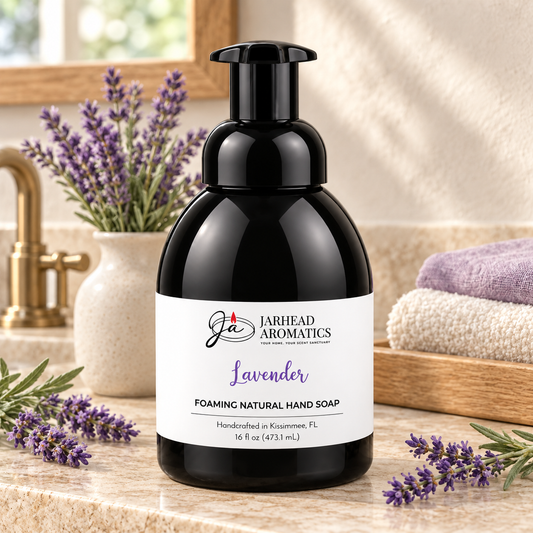 A black bottle of Lavender Handmade Foaming Natural Hand Soap by Jarhead Aromatics sits on a bathroom counter next to lavender sprigs and folded towels.