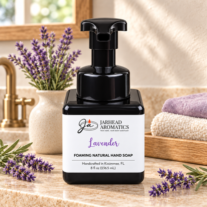 Black foaming bottle of Jarhead Aromatics Lavender Handmade Foaming Natural Hand Soap sitting on a bathroom counter with sprigs of lavender and folded towels.