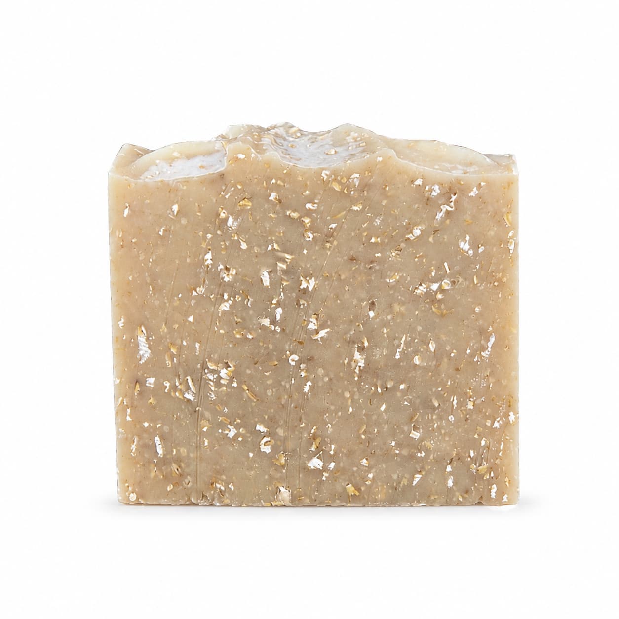 A rectangular bar of Jarhead Aromatics’ Lavender + Oatmeal Handmade Natural Goat Milk Artisan Soap, featuring a natural beige hue with visible flecks and an uneven top edge, stands upright on a plain white background.