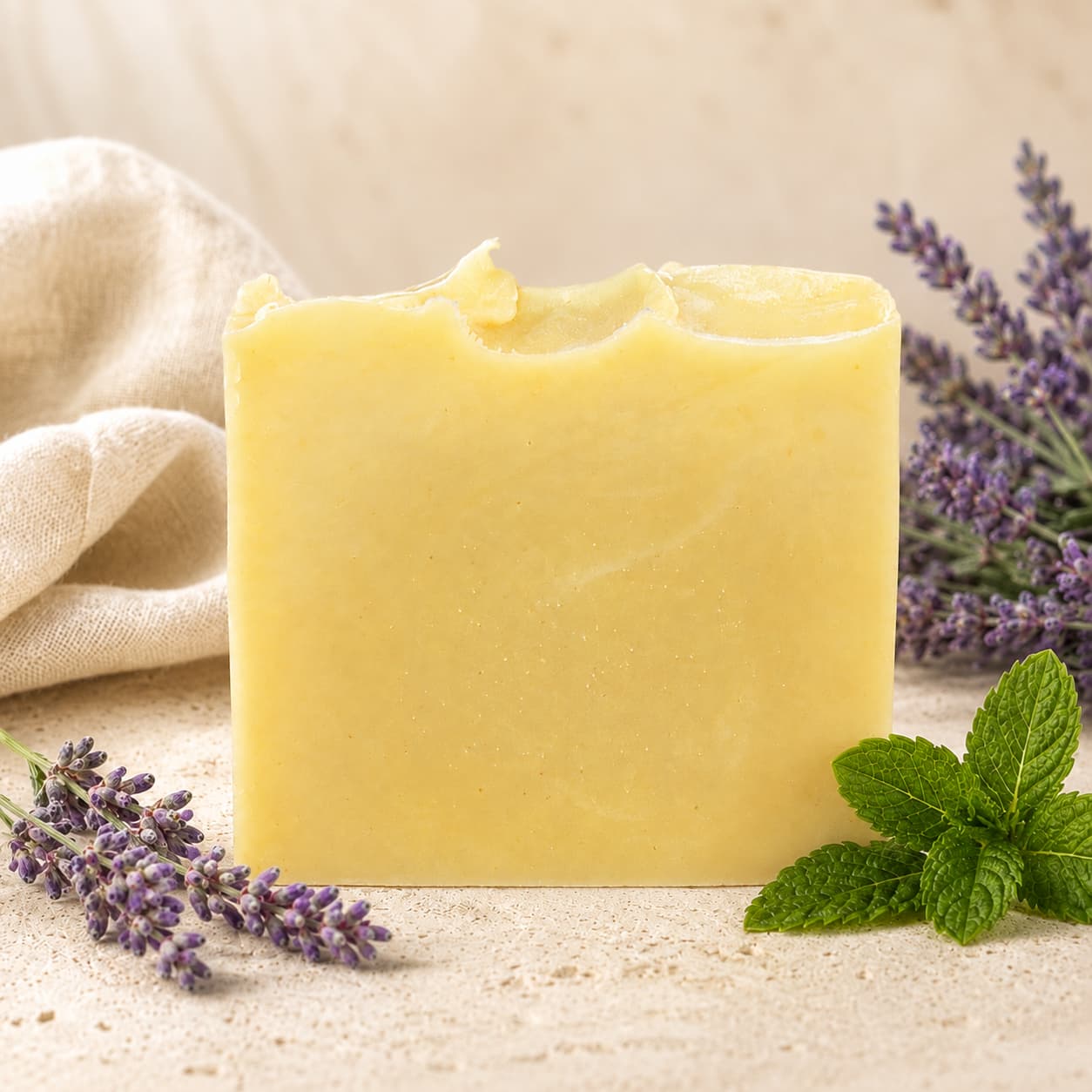 A bar of Jarhead Aromatics Lavender + Peppermint Handmade Natural Artisan Soap stands upright on a light surface, surrounded by sprigs of lavender and mint leaves, with a beige cloth in the background.