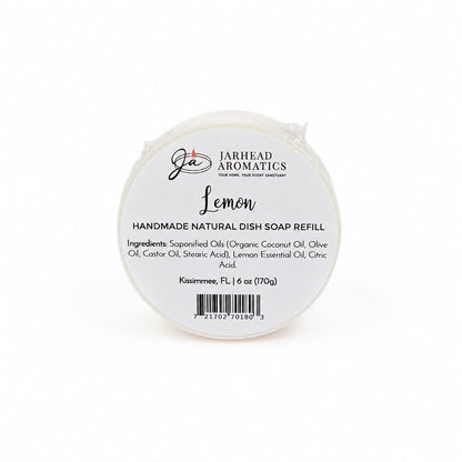 A round white soap bar labeled "Jarhead Aromatics Lemon Handmade Natural Solid Dish Soap | Citrus Kitchen Cleaning Bar with Lemon Essential Oil," featuring a list of ingredients, weight (6 oz), barcode, and citrus scent details. This plant-based lemon solid dish soap is ideal for kitchen cleaning.