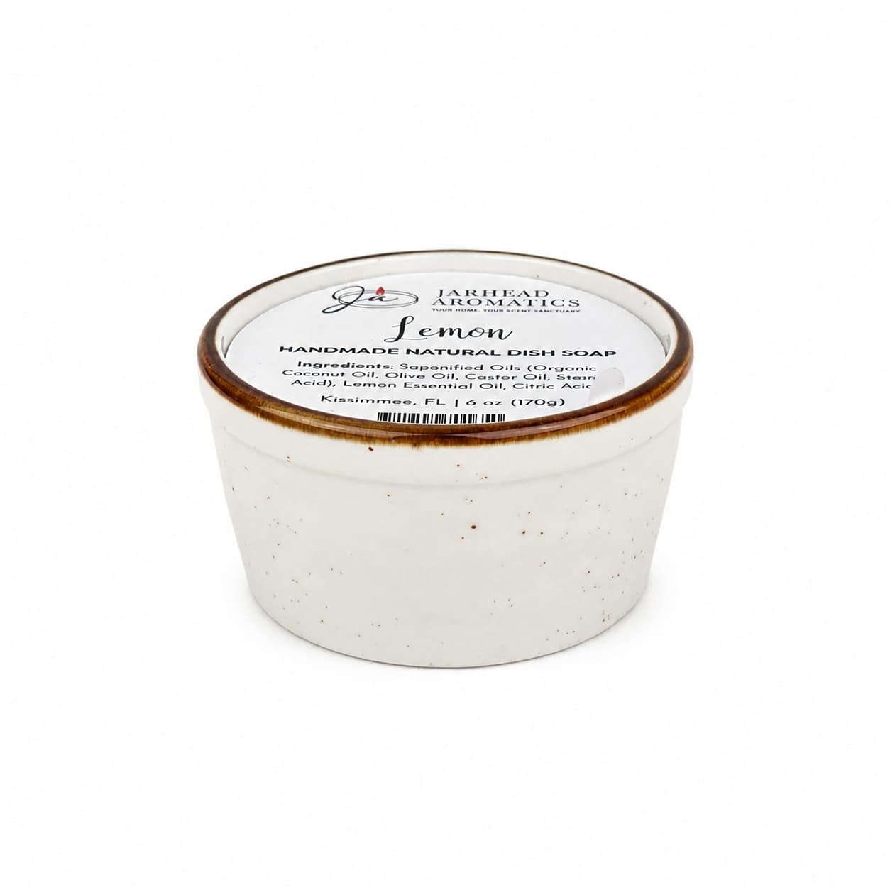 A white ceramic container with a lid labeled Lemon Handmade Natural Solid Dish Soap from Jarhead Aromatics, featuring a plant-based formula with lemon essential oil and displaying ingredients and brand information on the top.