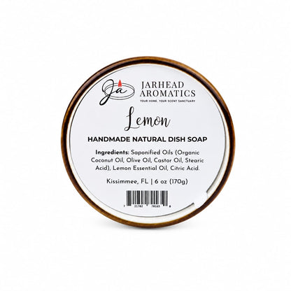 A round container labeled "Jarhead Aromatics Lemon Handmade Natural Solid Dish Soap | Citrus Kitchen Cleaning Bar with Lemon Essential Oil," listing ingredients and weight, sits against a white background. This plant-based dish soap bar offers a refreshing lemon aroma and a solid formula for an eco-friendly kitchen clean.