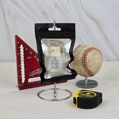 A resealable black pouch, red triangular ruler, worn baseball on a stand, and yellow tape measure are arranged on a marble-patterned background, highlighting Jarhead Aromatics' The Lumberjack Car Diffuser—an outdoorsy cedar, oak & mahogany air freshener.