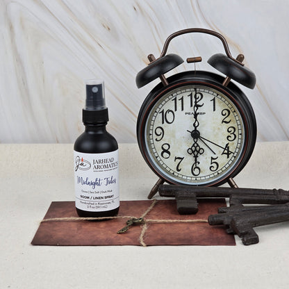 A vintage alarm clock sits beside a bottle of Jarhead Aromatics Midnight Tides Room & Linen Spray—Sea Salt, Dark Musk & Sandalwood—old keys, and a tied brown envelope, bringing a soothing coastal scent and timeless home fragrance to the scene.