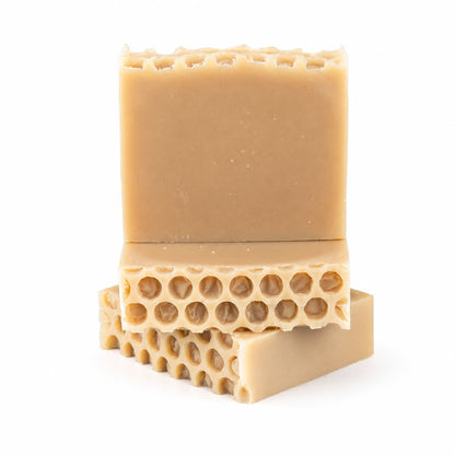 Three beige bars of Jarhead Aromatics’ Milk + Honey Handmade Natural Goat Milk Artisan Soap are stacked, each showcasing a honeycomb-like pattern on one side. The creamy, natural soap bars are set against a plain white background.