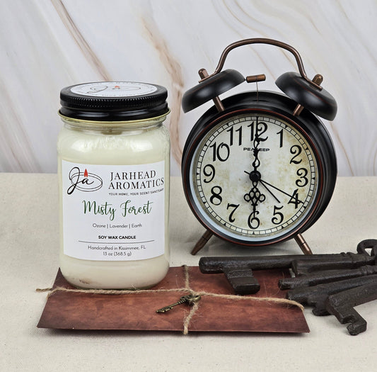 The Misty Forest - Soy Wax Candle by Jarhead Aromatics fills the air with freshness, accompanied by a vintage-style alarm clock. Several rustic keys lie on vintage brown paper, creating a nostalgic and tranquil ambiance.