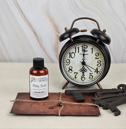 A vintage-design alarm clock sits beside a small bottle labeled Misty Forest - Reed Diffuser Refill by Jarhead Aromatics, offering an earthy fragrance. Two large metal keys rest on brown paper tied with string, all displayed on a light-colored surface.