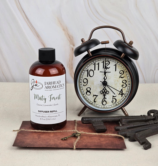 A Jarhead Aromatics Misty Forest - Reed Diffuser Refill, offering a woodsy fragrance with hints of ozone, lavender, and earth, accompanies an antique-style alarm clock. A brown envelope holding vintage keys tied with twine lies in front.