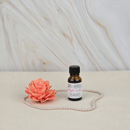 A small amber bottle of Jarhead Aromatics’ Mystic Orchid Cold Air Diffuser Refill (Coastal Floral & Vanilla) sits on a light surface with a pink artificial flower, pearls, and a marble-patterned background.