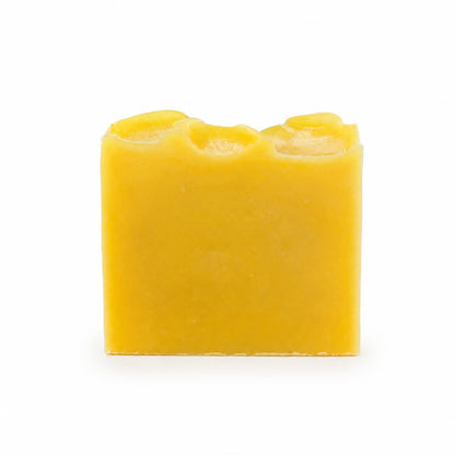 A rectangular yellow bar of Jarhead Aromatics Orange + Carrot Handmade Natural Artisan Soap, featuring a wavy, uneven top edge and set against a plain white background.