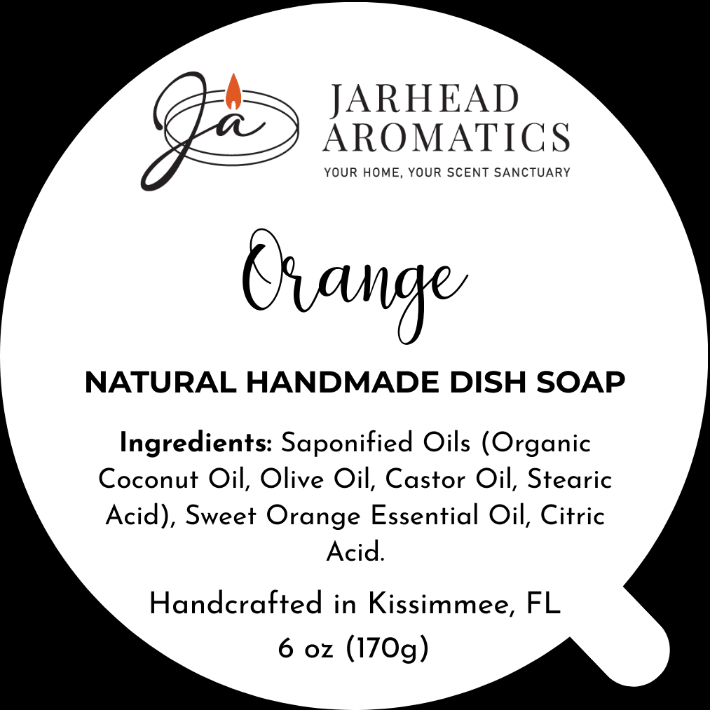 A round black and white label for Jarhead Aromatics Orange Handmade Natural Solid Dish Soap lists ingredients, features orange text, a stylized Ja logo, notes it's handcrafted in Kissimmee, FL, and highlights its plastic-free solid dish soap formula.