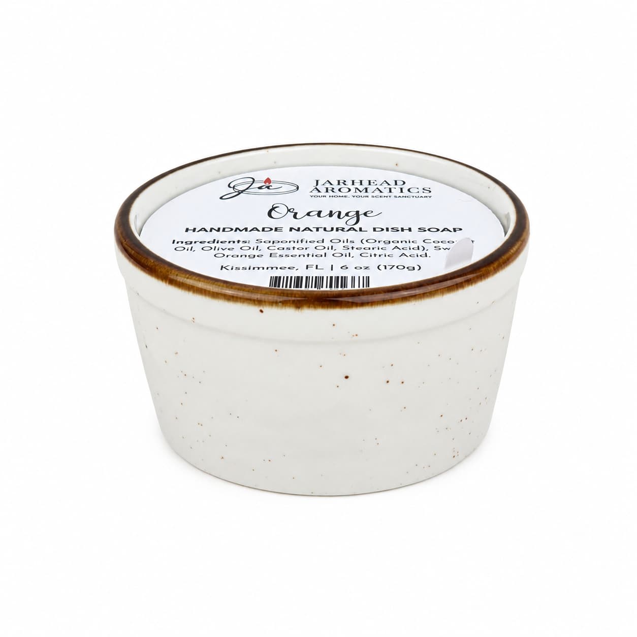 A white ceramic jar with a brown rim holds Jarhead Aromatics Orange Handmade Natural Solid Dish Soap—a citrus kitchen cleaning bar with essential oils, labeled "Orange." The lid displays the ingredient list and the size as 6 oz (170g).