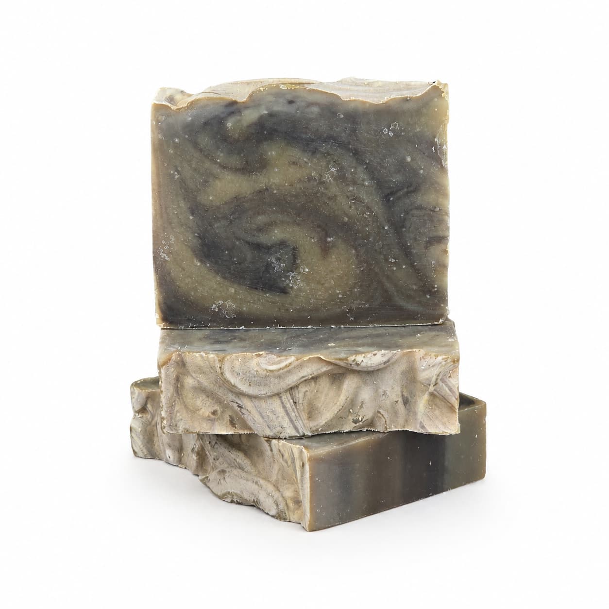 Three rectangular bars of marbled, handcrafted soap in shades of gray, olive, and cream are stacked on a white background. The rustic, swirled patterns and wavy edges showcase the artisanal quality of each bar from Jarhead Aromatics. Among these distinctive creations is our Palo Santo + Patchouli Handmade Artisan Soap | Smoky Woodsy Charcoal Soap—a unique blend of earthy aromas and striking design, ideal for thoughtful gifting or everyday indulgence.