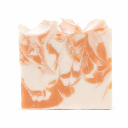 A rectangular bar of Jarhead Aromatics Peach + Magnolia Handmade Coconut Milk Artisan Soap features a marbled pattern of cream and orange swirls with wavy, uneven top edges, set against a plain white background.