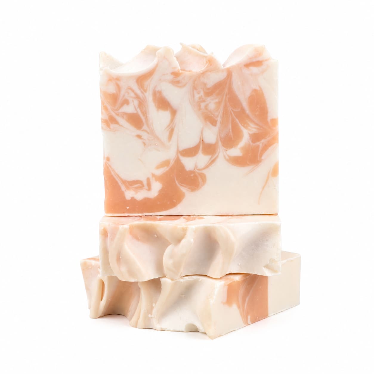 Three artisanal soap bars, including the Peach + Magnolia Handmade Coconut Milk Artisan Soap from Jarhead Aromatics, showcase a white and peach marbled design as they are stacked against a white backdrop. These Juicy Peach & Floral Magnolia soaps feature textured, wavy tops and a smooth, clean-cut appearance.