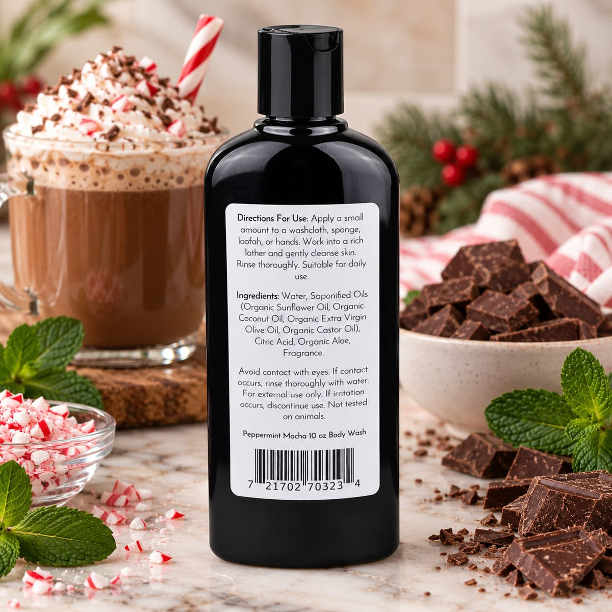 A black bottle of Jarhead Aromatics Peppermint Mocha Handmade Body Wash featuring a back label with ingredients and usage instructions, surrounded by a mug of hot cocoa, chocolate chunks, peppermint bits, and mint leaves.